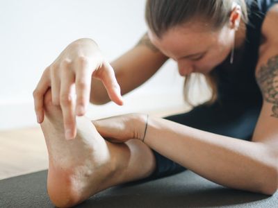 Woman performing a gentle stretching pose on a yoga mat indoors.